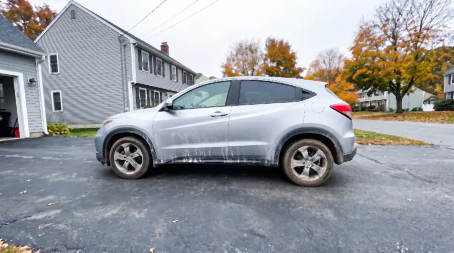 Illustration of a silver crossover SUV on a suburban driveway before a detail: white road-salt streaks down the doors, grey road film flattening the paint, mud sprayed up the wheel arches, wheels grey with brake dust.