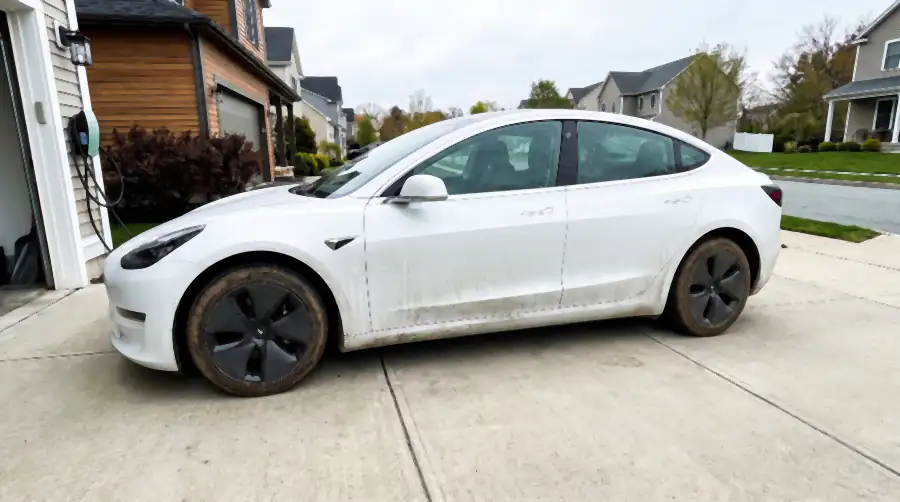 Illustration of a white electric sedan on a driveway before a detail: a grey-brown film of road grime dulling the white paint, heavy salt streaks down the lower doors and behind the wheels, grey wheel faces, hazy glass.