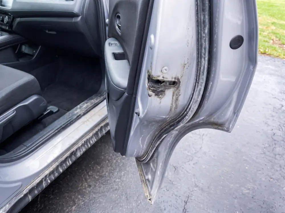 Illustration of a door jamb before cleaning: a thick black line of grime and salt packed along the seal channel and into the corners, the rubber weather seal grey and chalky, the striker caked with dirty grease.
