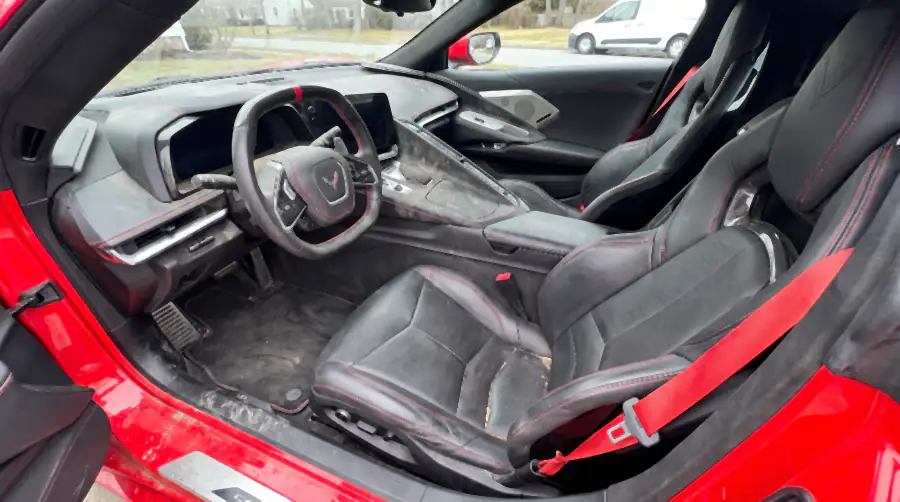 Illustration of the same coupe's cabin before an interior detail: dust settled over the dashboard and the tall centre console, grit in the leather seams and the seat bolsters, marks on the sill plate from climbing over it.