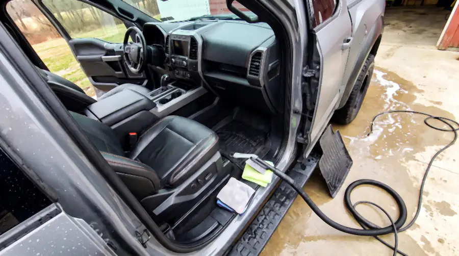 Illustration of the same cab after an interior detail: leather evenly clean, rubber mat scrubbed deep black with water still beading on it, fresh vacuum lines in the carpet, side step wiped. The extractor hose runs out of the door and a mat leans drying against the running board.