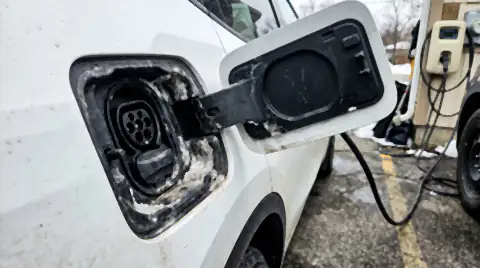 The open charging port on the rear quarter of a white electric car, with white road salt crust built up around the rubber port seal.