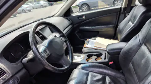 The cabin of a shared pool car: a worn shiny seat bolster, a scuffed steering wheel and cup holders ringed with old coffee.