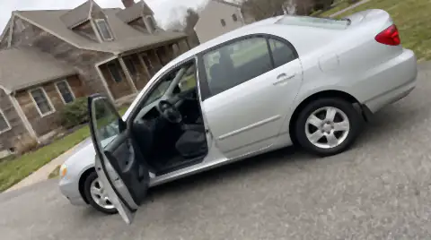 A clean used saloon photographed side-on in a driveway with its driver door open, the way a car is photographed for a private sale listing.
