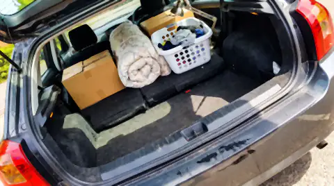 A hatchback with the rear seats folded and packed with moving boxes and bedding, with scuff marks along the boot sill trim.
