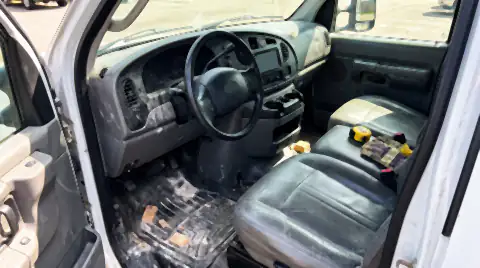 The cab of a working trades van: a rubber floor mat covered in dust and offcuts, a dusty dashboard and tools on the passenger seat.