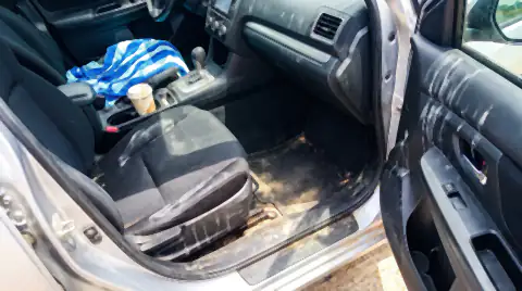 A car interior after a lake day: sunscreen smears on the door card, a damp towel on the back seat and sand in the footwell carpet.