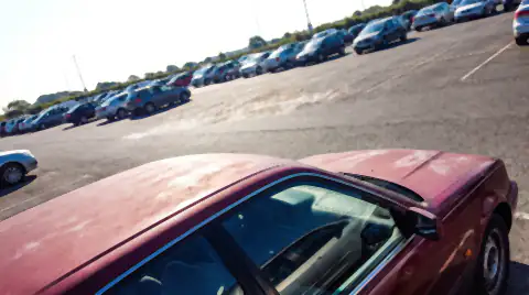 The roof and bonnet of a dark red car in an open car park under hard midday sun, the horizontal panels visibly dull and sun-faded.