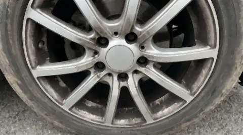 An alloy wheel face caked in thick black brake dust, with the caliper and scored disc visible behind the spokes.